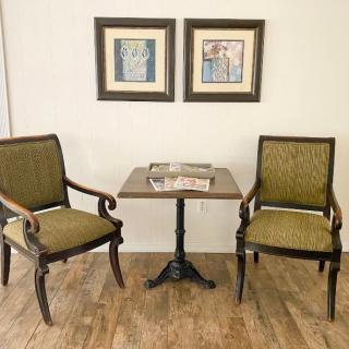A cozy seating area with two upholstered chairs and a small table,
 complemented by framed artwork on the wall.