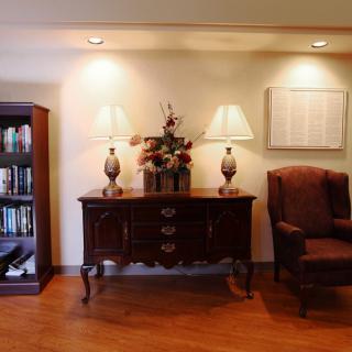 A cozy living room setup featuring an elegant wooden sideboard with table lamps, a decorative vase, and an armchair next to a bookshelf.