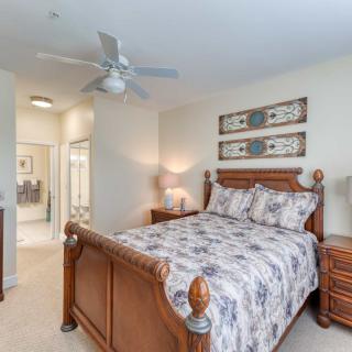 A cozy bedroom with a wooden bed frame, floral bedding, and matching bedside tables under artwork and a ceiling fan.
