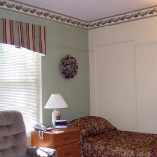 A cozy bedroom with a single bed, a nightstand with a lamp, and a window with blinds.