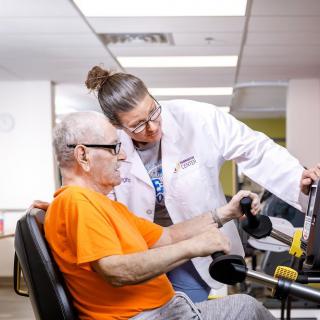 A healthcare professional assists an elderly man in physical therapy exercises.