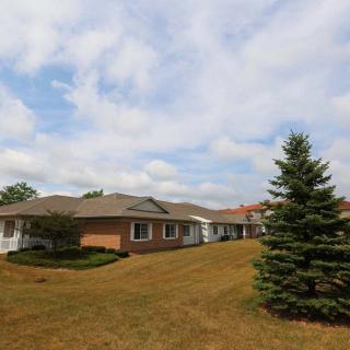 A suburban house with a large grassy yard and scattered trees under a cloudy sky.