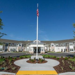 A modern building with a central entrance and an American flag on a flagpole surrounded by landscaping.