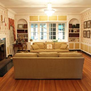 A cozy living room with a sofa facing a fireplace, surrounded by bookshelves and decorated walls.