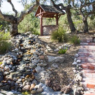 A tranquil garden scene featuring a stone path, a rustic well, and surrounding greenery.