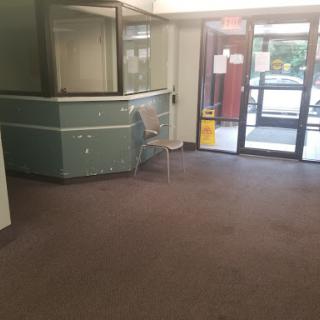 A spacious and empty lobby area featuring a reception desk, adjacent to a glass entrance.