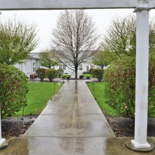 A wet pathway beneath an archway leads through a garden area with trees and bushes.