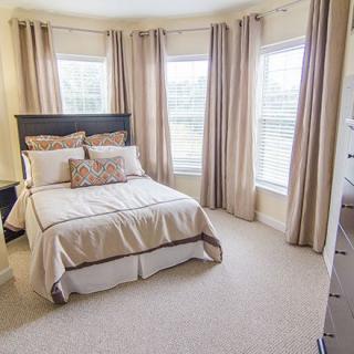 A cozy bedroom with neutral tones and large windows.
