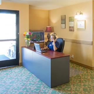 A receptionist sitting at a desk in a waiting area, using a laptop and phone.