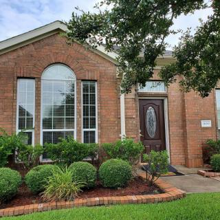 A brick house with a manicured front yard featuring shrubs and a tree.