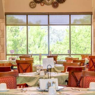 A bright and cozy restaurant dining area with tables and chairs, illuminated by natural light from large windows.
