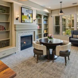 A cozy living room with a fireplace, surrounded by bookshelves and featuring a round table with chairs.