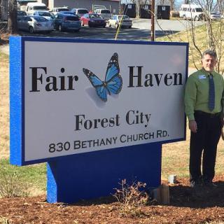 A person standing next to a sign for Fair Haven located on Bethany Church Rd in Forest City.
