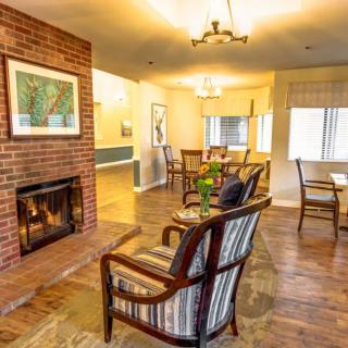 A cozy living room with a brick fireplace and comfortable seating, featuring a dining area in the background.