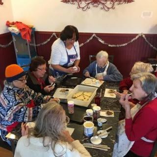 A group of elderly people socializing and participating in a baking activity around a table.