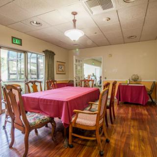 A well-lit dining room with a large table and wooden chairs, featuring a red tablecloth and a wooden floor.