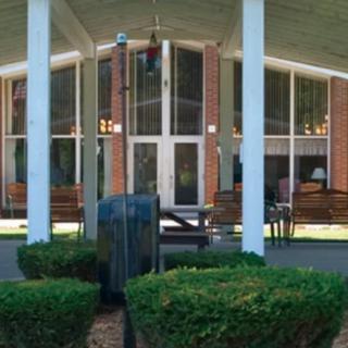 A building entrance with large windows and tall columns, framed by neatly trimmed bushes.