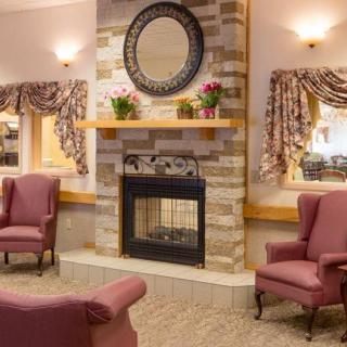 A cozy living room with a fireplace, surrounded by pink armchairs and decorated with a mirror above the mantel.