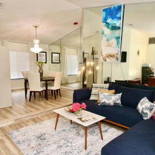 A modern and cozy living room with a blue sofa, wooden flooring, and a dining area in the background.