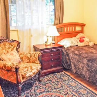 A cozy bedroom with a single bed, ornate armchair, and a wooden nightstand featuring a lamp.