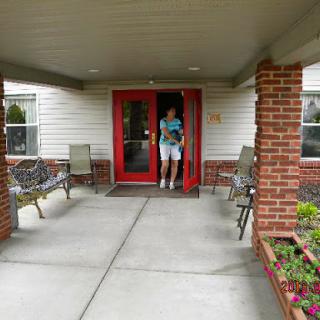 A person exiting through a red door into a well-maintained outdoor area with seating and flower beds.