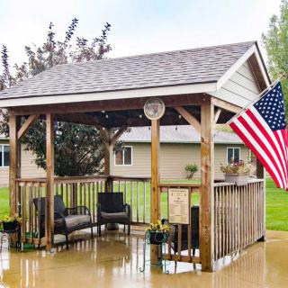 A wooden gazebo with outdoor furniture and an American flag displayed, surrounded by a suburban neighborhood.