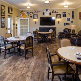 A cozy recreation room with tables, chairs, and a large television, decorated with various wall memorabilia.