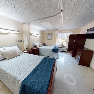 A view of a patient room featuring two beds and essential furnishings in a hospital setting.