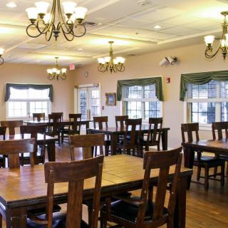 An empty dining room with wooden tables and chairs, featuring chandeliers and large windows.