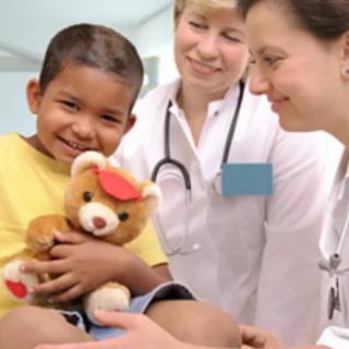 A child holding a teddy bear is comforted by two doctors during a healthcare visit.