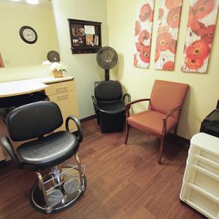 A cozy hair salon room with chairs, a hair dryer, and decorative art on the walls.