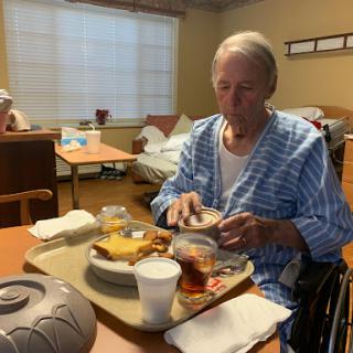 An elderly person enjoying a meal in an assisted living facility.