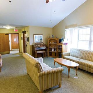 A cozy living room featuring sofas and a coffee table, with a bookshelf and piano in the corner.