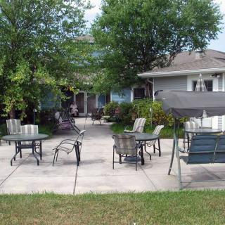 A cozy patio area with outdoor seating, surrounded by lush greenery and a house in the background.