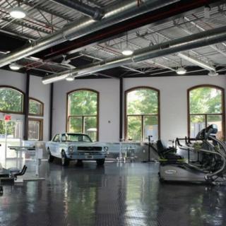 A vintage car displayed in an industrial-style garage with large windows.