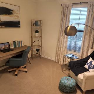 A cozy home office with a desk, armchair, and bookshelf near a window.