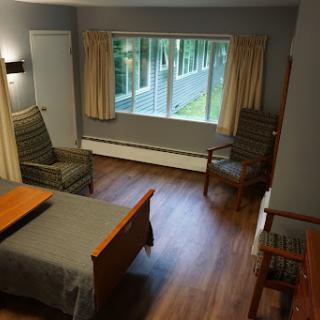 A cozy interior of a room featuring a bed, two chairs, and a large window with curtains.
