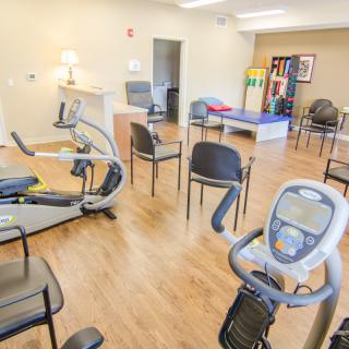 A well-lit exercise room equipped with various machines and chairs for therapy.