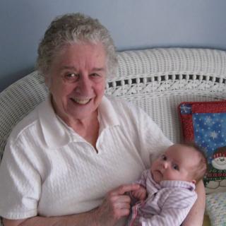 An elderly woman is happily holding a baby indoors.