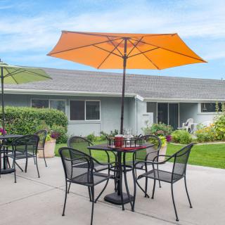 A patio with tables and chairs under orange umbrellas in a garden setting.