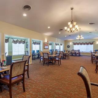 A spacious dining room featuring multiple tables and chairs, illuminated by elegant chandeliers.