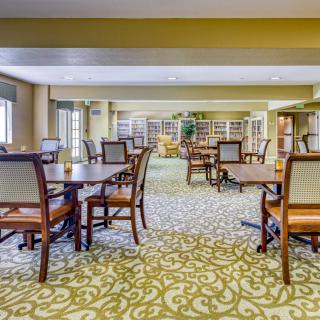 A well-lit dining area with arranged tables and chairs, featuring a patterned carpet.