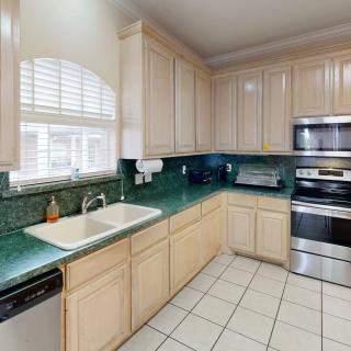 A modern kitchen with light wooden cabinets, green countertops, and stainless steel appliances.