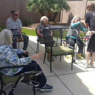 A group of seniors enjoying a sunny day outdoors, seated in chairs during a social gathering.