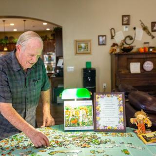 An elderly man working on a jigsaw puzzle at home.