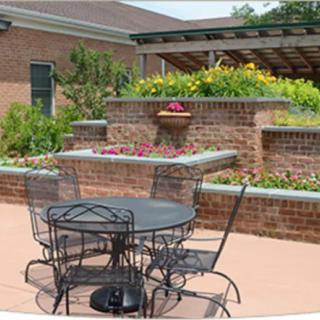 A cozy outdoor patio with a metal table and chairs, surrounded by a brick wall and lush plants.