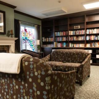 A cozy library reading room featuring comfortable armchairs, a fireplace, and shelves filled with books.