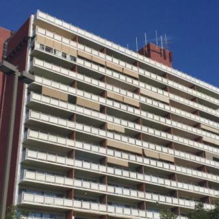 A tall residential apartment building with multiple balconies against a clear blue sky.