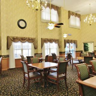 A well-lit dining room with elegant chandeliers and neatly arranged tables and chairs.