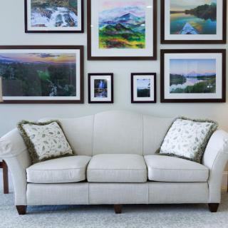 A cozy living room with a white sofa adorned with patterned cushions and a wall decorated with various landscape paintings.